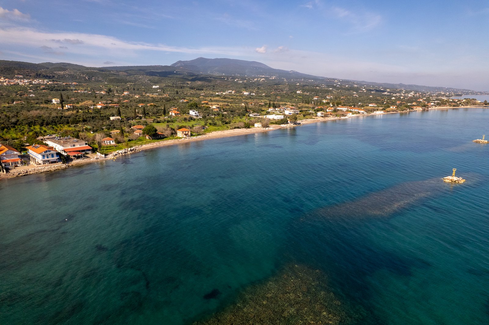 "Aerial view of Kafou, Greece coastline with clear turquoise waters, sandy beaches, and a picturesque village set against lush green hills