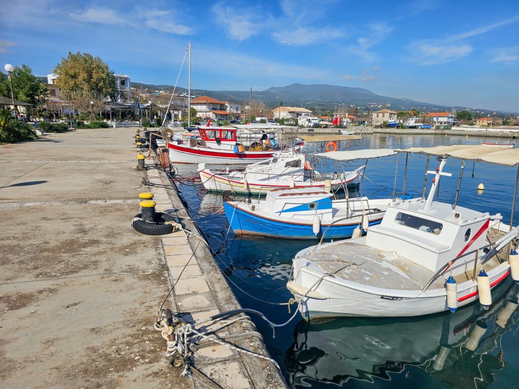 Traditional fishing boats docked at the harbor in Kafou, Greece, with a scenic mountain backdrop